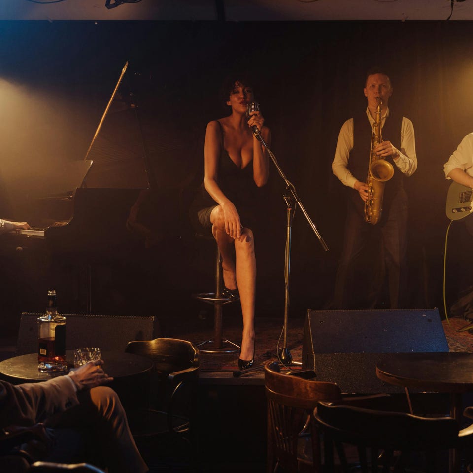 A jazz band performs live on stage in a dimly lit club with a singer and musicians playing various instruments.