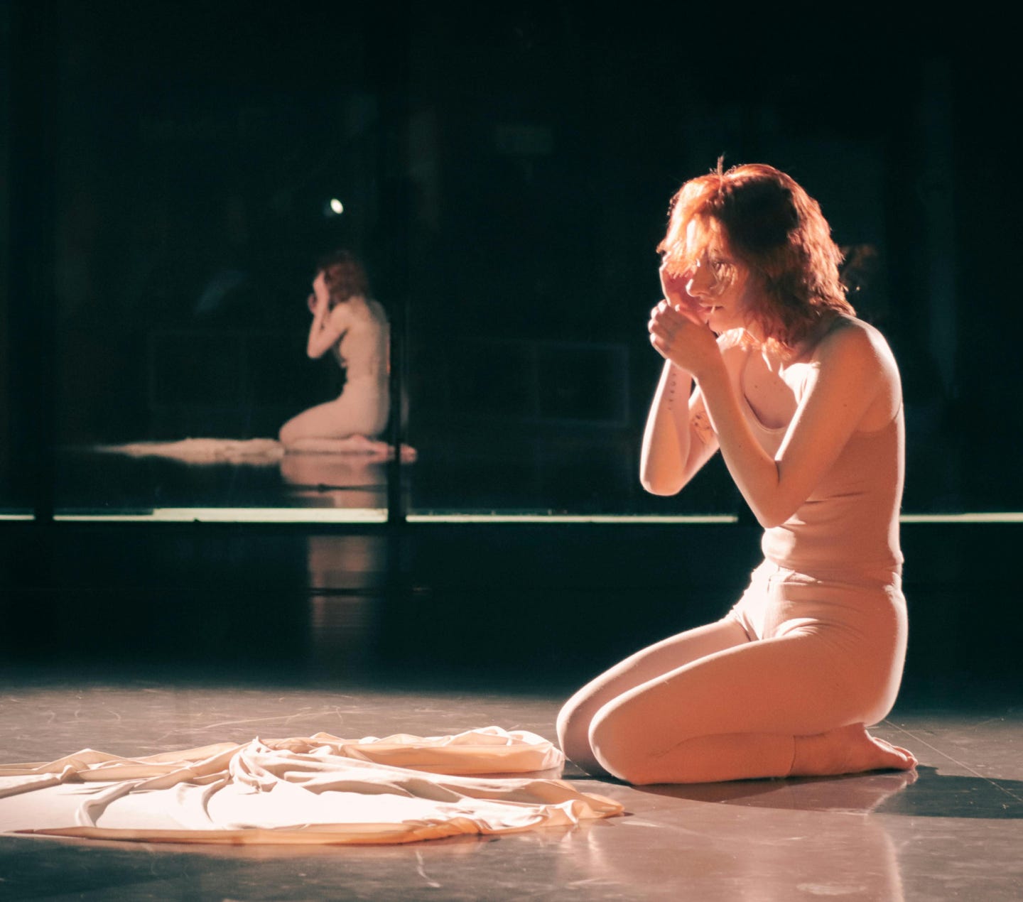 A woman expressing deep emotion during a dance rehearsal in a dimly lit studio.