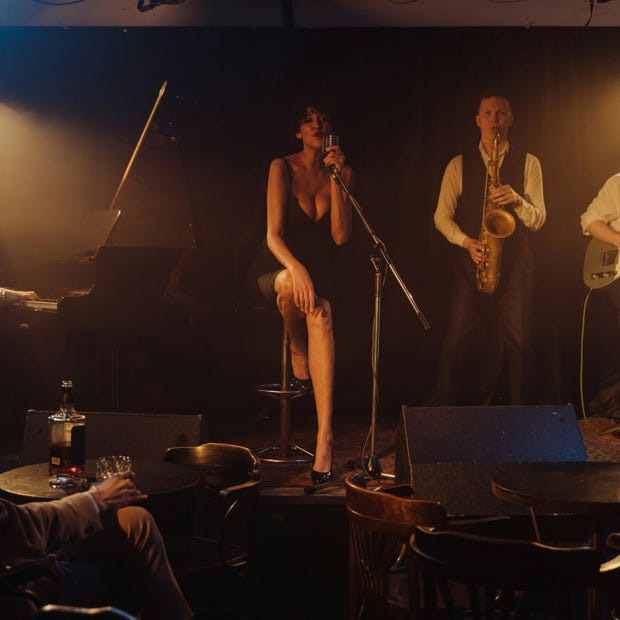 A jazz band performs live on stage in a dimly lit club with a singer and musicians playing various instruments.